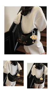 Détail du sac hobo croissant noir avec broderie orange et charm de poupée en peluche