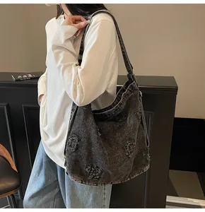 Detailed view of large washed denim tote bag with letter patches worn on the shoulder