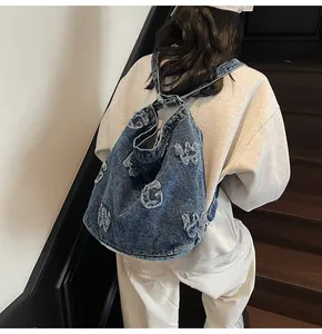 Detail of blue denim bucket bag featuring white distressed letter patterns and metal rings