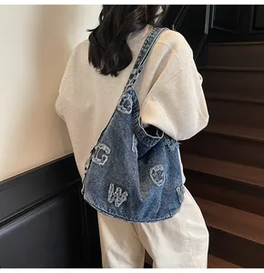 Detail of vintage washed denim tote bag showing frayed letter embroidery and metal rings