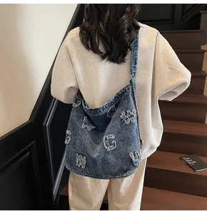 Detail of blue washed denim tote bag with white fringed letter patches on stairs
