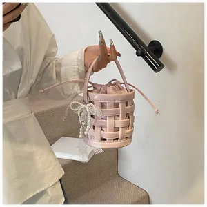Dettaglio borsa a secchiello intrecciata rosa con fiocco in pizzo e ciondolo di perla