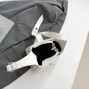 Sac seau blanc avec clous argentés et bandoulière réglable sur un fond gris neutre
