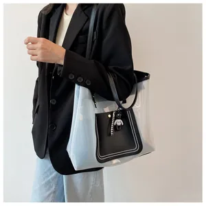 Detailed side view of large transparent PVC tote bag with black leather trim and bear charm