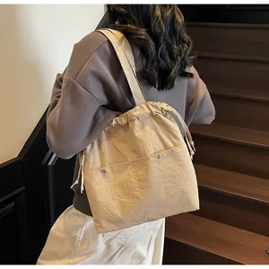 Detail of beige nylon drawstring tote showing dual front pockets and adjustable side cords