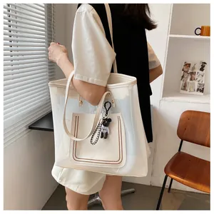 Detail of white mesh tote bag with leather pocket and bear charm on model shoulder