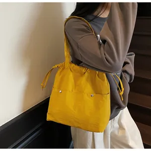 Detail of yellow nylon tote bag featuring front snap pockets and drawstring closure