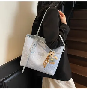 Dettaglio della borsa tote azzurra con ricamo floreale bianco e ciondolo a forma di orso