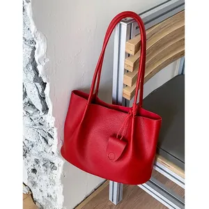 Chic red leather tote bag with lychee texture and mini charm on a wooden bench