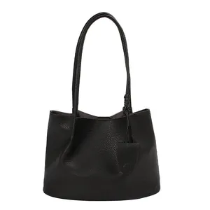 Minimalist black pebble leather tote bag with long shoulder straps and knot charm