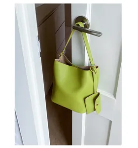 Détail d'un sac seau en cuir vert clair à texture litchi suspendu à une poignée de porte