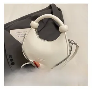 Close-up of a white half-moon mini bag with ring handle, knot detail and chain strap
