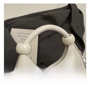 Detail view of smooth leather handle and silver zipper on minimalist off-white crescent bag