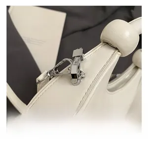 Detailed close-up of polished silver metal hooks and white leather texture on handbag