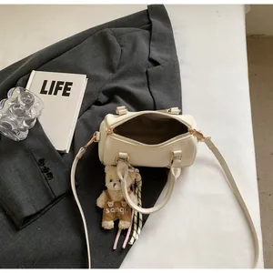 Fashionable cream cylinder Boston bag with teddy bear pendant on grey blazer