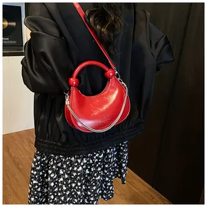 Red glossy patent leather crescent bag with chain strap and top handle shown on model