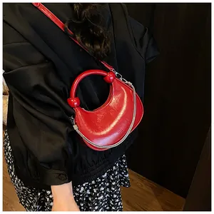 Detail of red crescent leather bag featuring a round handle and silver chain strap