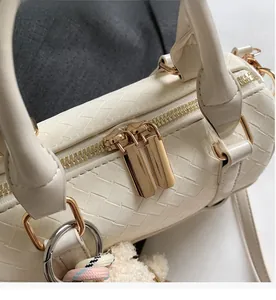 Detail of smooth gold double zippers on a cream woven leather handbag with bear charm