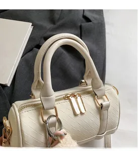 Detail of cream woven Boston bag with gold zippers and a plush ball charm on grey fabric