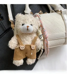 Detail of cream plush teddy bear charm with corduroy overalls on a woven handbag