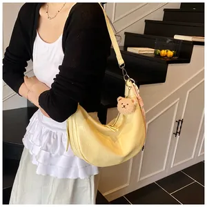 Detail of pale yellow crocodile texture crescent shoulder bag with plush bear charm