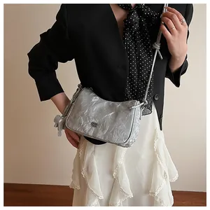 Silver metallic crossbody bag with textured pleats and floral charm worn by a model