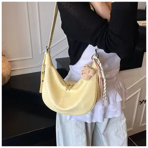 Detail of pale yellow hobo bag with crocodile pattern and a cute plush bear charm