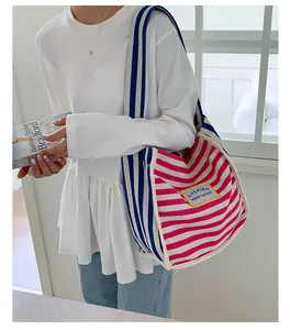 Detail of pink and blue striped canvas tote bag with a wide shoulder strap worn by model