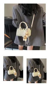 Detail view of light green Boston bag with woven texture, white handles and bear charm