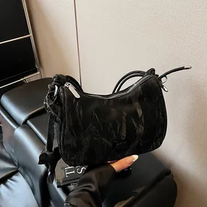 Minimalist black pleated crescent shoulder bag with knot detail on high-quality leather sofa