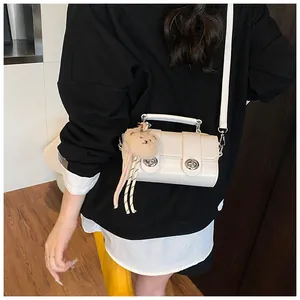 Detail view of white croc-embossed small square bag with cute brown plush bear charm