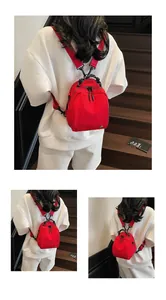 Detail view of a stylish red nylon mini backpack worn by a model in white attire