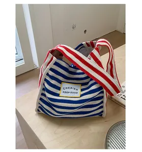 Close-up of blue striped canvas tote bag with red handles and slogan patch detail