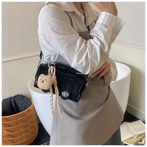 Detail of black crocodile texture shoulder bag with a cute brown plush bear charm