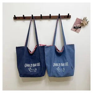 Detail of denim tote bag with red checkered lining and dachshund print hanging on hooks