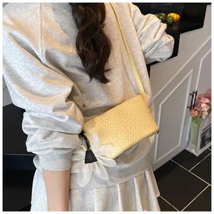 Détail du sac bandoulière jaune clair avec texture tressée et breloque marguerite