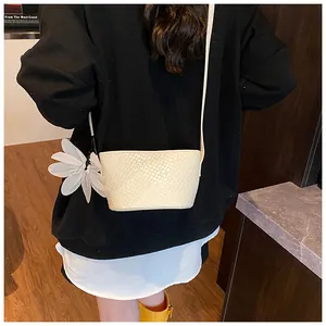 Détail du sac seau blanc à texture tressée avec breloque fleur et bandoulière fine