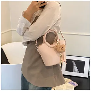 Detail of pink faux leather bucket bag with teddy bear charm and striped strap accessory