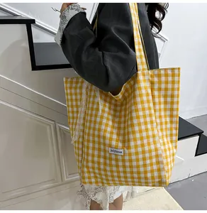 Detail of yellow checkered canvas tote bag featuring white lace edges and branded label