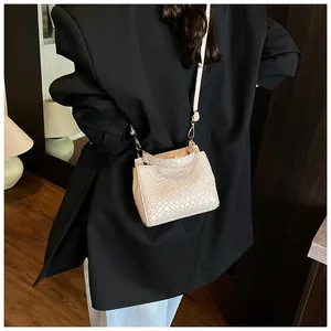 Détail du sac bandoulière crème avec texture crocodile porté sur un blazer noir