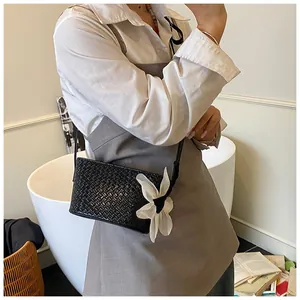 Détail du sac bandoulière tissé noir avec une décoration florale blanche artistique sur le côté