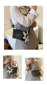 Détail du sac seau tressé noir avec une grande fleur blanche en tissu et bandoulière