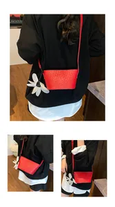 Détail d'un sac seau tressé rouge avec breloque fleur blanche et bandoulière fine