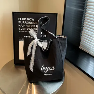 Minimalist black canvas tote bag with white lace bow and artistic lettering print