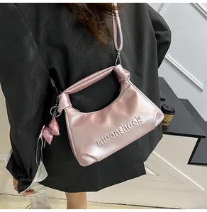 Détail d'un sac hobo rose métallisé avec poignée nouée, logo embossé et nœud décoratif