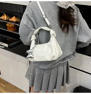 Détail du sac dumpling blanc brillant avec logo gaufré et pendentif nœud argenté