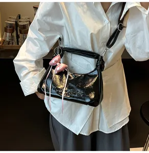 Détail du sac dumpling noir brillant avec relief et nœud rose porté à l'épaule
