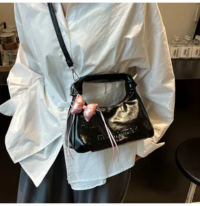 Détail du sac à main noir brillant avec nœud en satin rose et lettres embossées