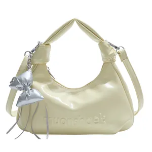 Sac hobo jaune crème avec breloque nœud argenté et poignée nouée sur fond blanc