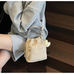 Detail of beige nylon drawstring bucket bag with adjustable strap and cloud plush charm